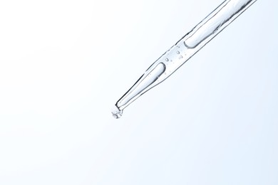 Dripping liquid from pipette on light blue background, closeup