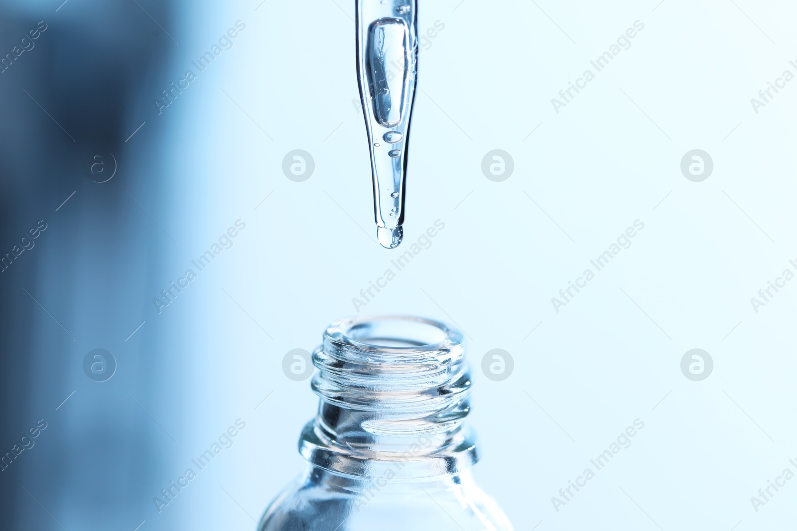 Photo of Dripping liquid from pipette into glass bottle on light blue background, closeup