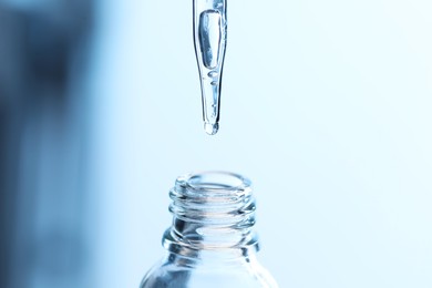 Dripping liquid from pipette into glass bottle on light blue background, closeup