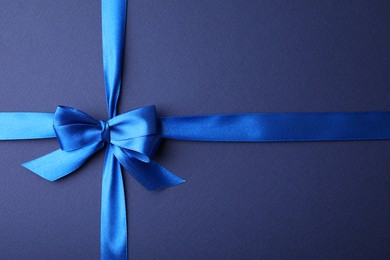 Photo of Bright satin ribbon with bow on blue background, top view