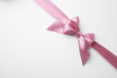 Photo of Pink satin ribbon with bow on white background, top view. Space for text