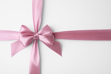 Pink satin ribbon with bow on white background, top view