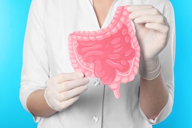 Photo of Doctor with paper intestine cutout on light blue background, closeup