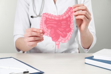 Doctor with paper intestine cutout at wooden table, closeup