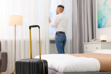 Photo of Guest opening curtains in stylish hotel room, focus on suitcase