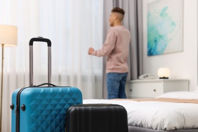 Guest opening curtains in stylish hotel room, focus on suitcases