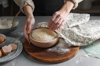 Photo of Woman covering dough with napkin at grey table, closeup