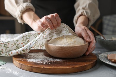 Photo of Woman covering dough with napkin at grey table, closeup