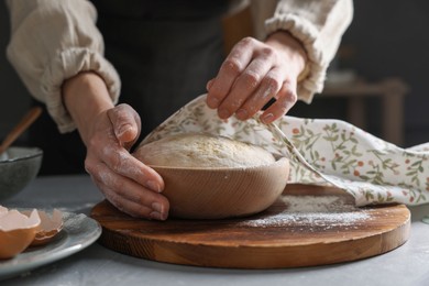 Woman covering dough with napkin at grey table, closeup