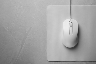 Wired mouse with mousepad on grey textured table, top view. Space for text