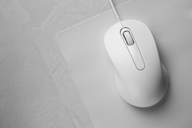 Photo of Wired mouse with mousepad on grey textured table, top view. Space for text