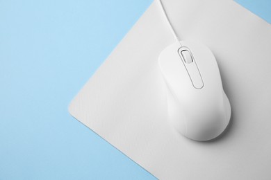 Wired mouse with mousepad on light blue background, top view. Space for text