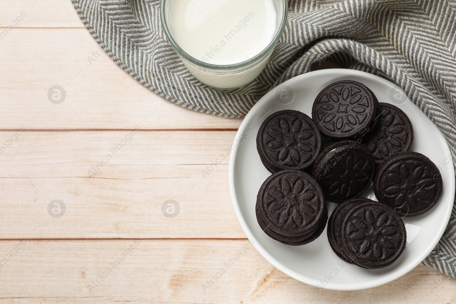 Photo of Plate with tasty sandwich cookies and milk on light wooden table, top view. Space for text