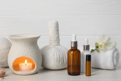Different aromatherapy products and burning candle on white table