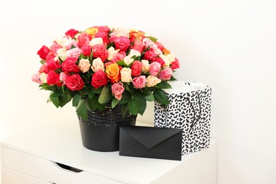 Bouquet of beautiful roses, envelope and shopping bag on white drawer unit