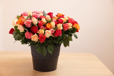 Photo of Bouquet of beautiful roses on wooden table against beige background