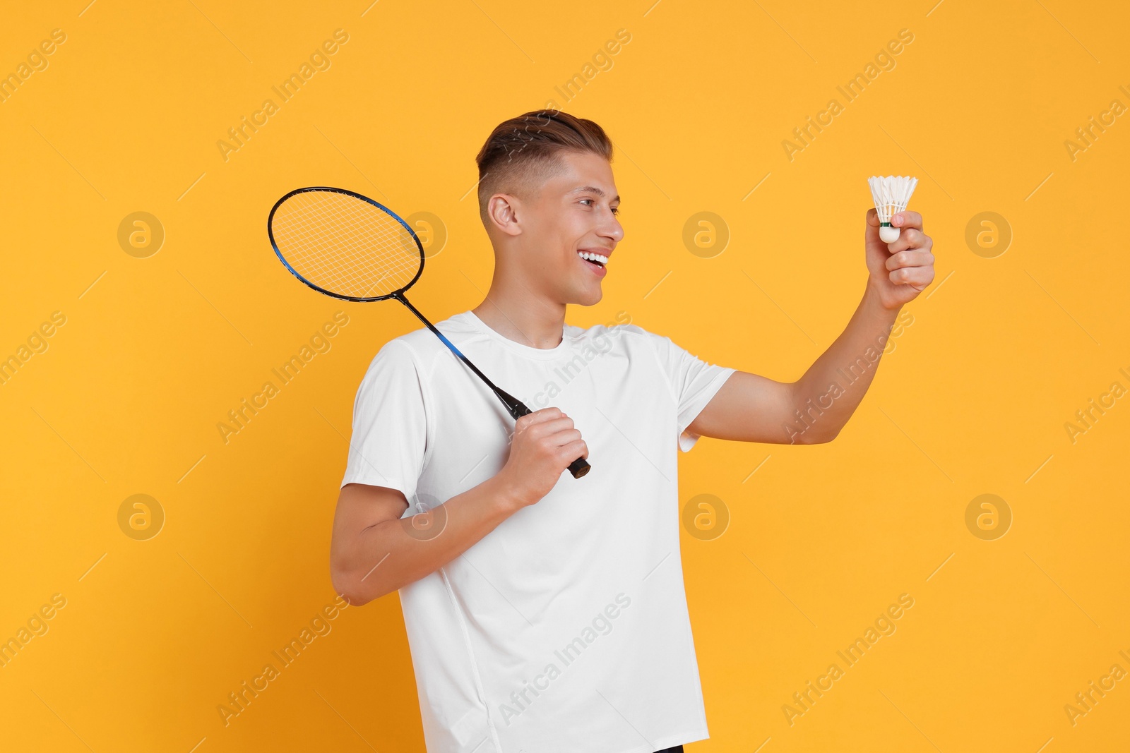 Photo of Young man with badminton racket and shuttlecock on orange background