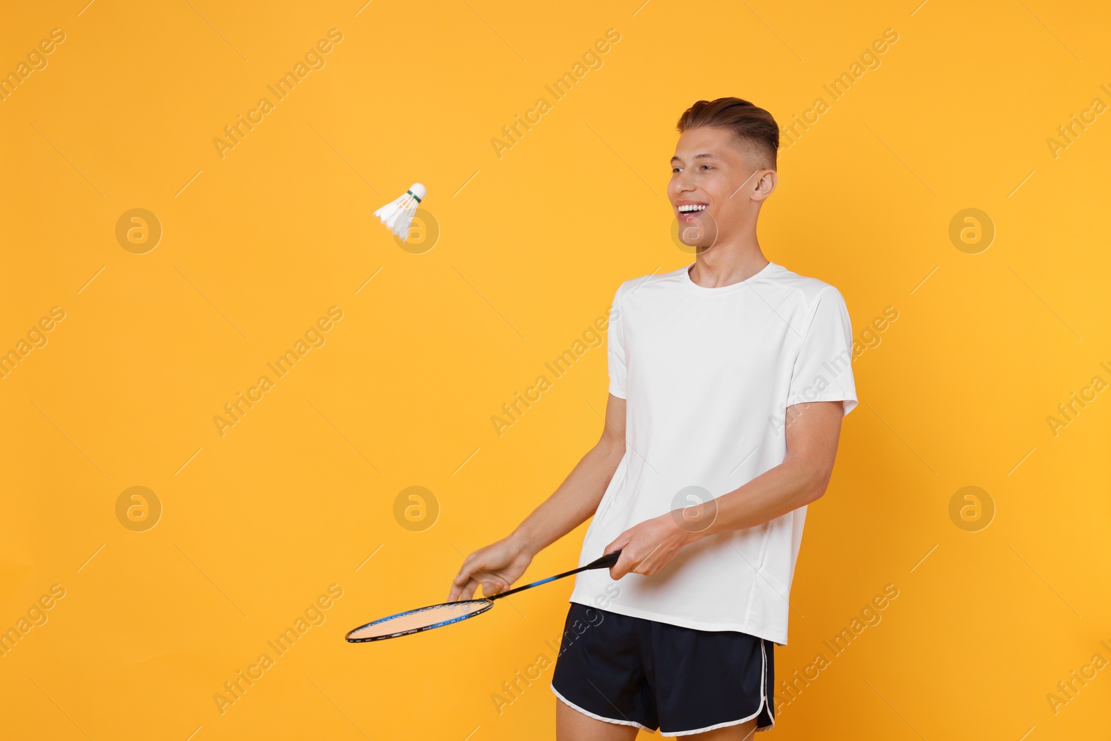 Photo of Young man with badminton racket and shuttlecock on orange background