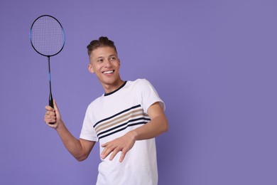 Young man playing badminton with racket on purple background