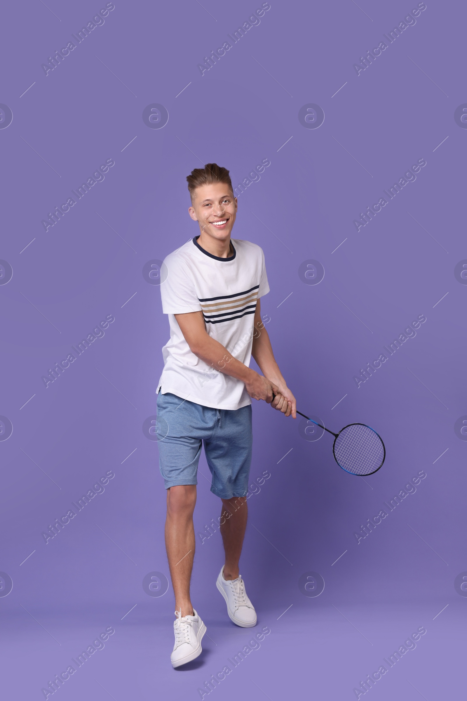 Photo of Young man playing badminton with racket on purple background