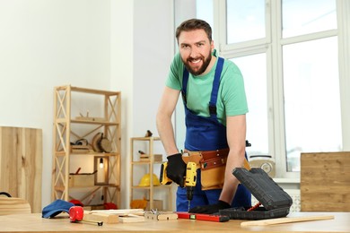 Photo of Smiling craftsman working with drill at wooden table in workshop