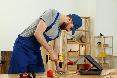 Photo of Craftsman working with drill at wooden table in workshop