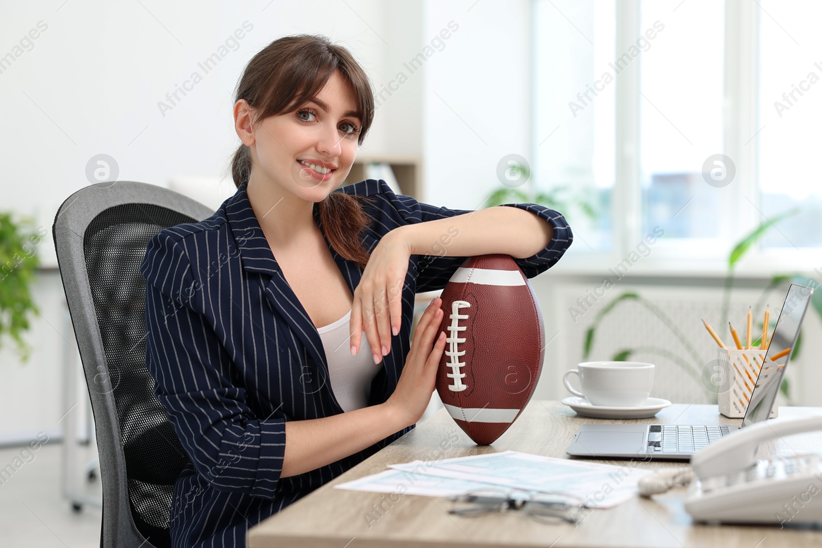 Photo of Smiling employee with american football ball at table in office