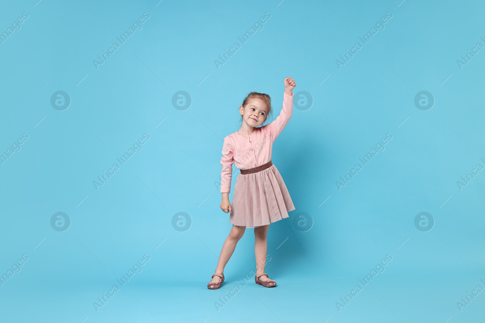 Photo of Cute little girl dancing on light blue background