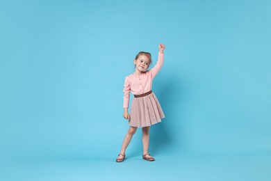 Cute little girl dancing on light blue background