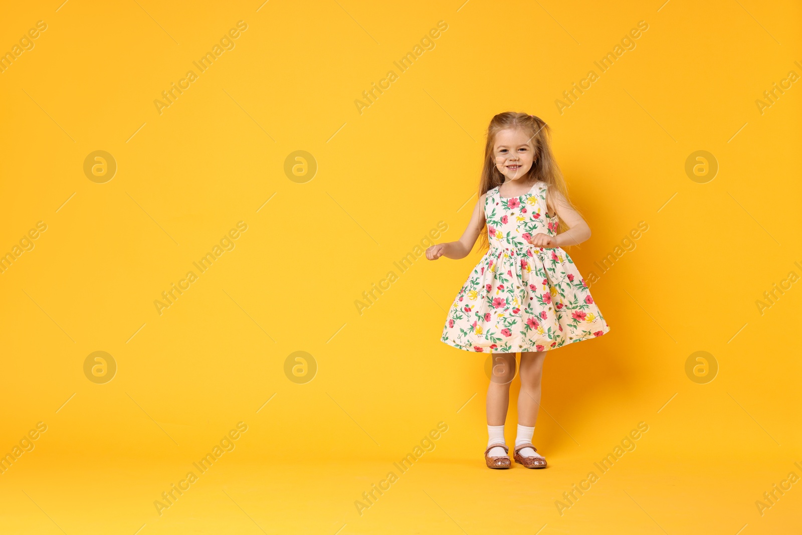 Photo of Cute little girl dancing on orange background, space for text