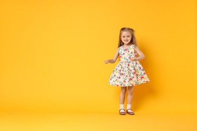 Photo of Cute little girl dancing on orange background, space for text