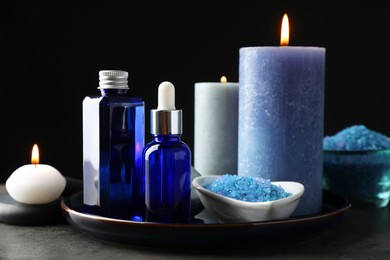 Photo of Spa composition. Cosmetic products, burning candles and sea salt on gray table against black background, closeup