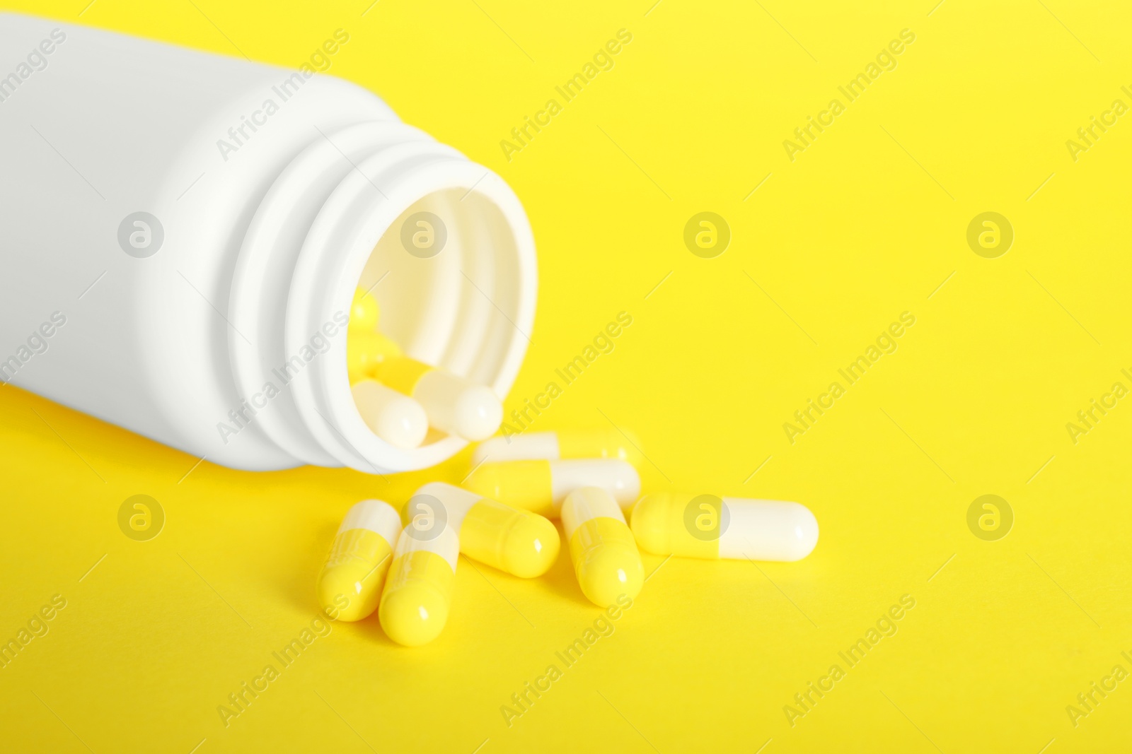 Photo of Scattered antibiotic pills and bottle on yellow background, closeup. Medicinal treatment