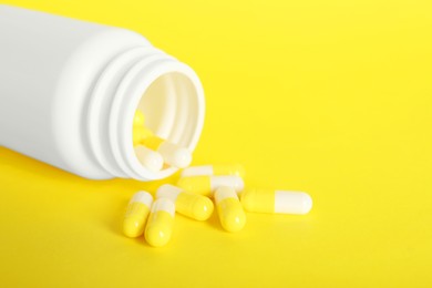 Photo of Scattered antibiotic pills and bottle on yellow background, closeup. Medicinal treatment