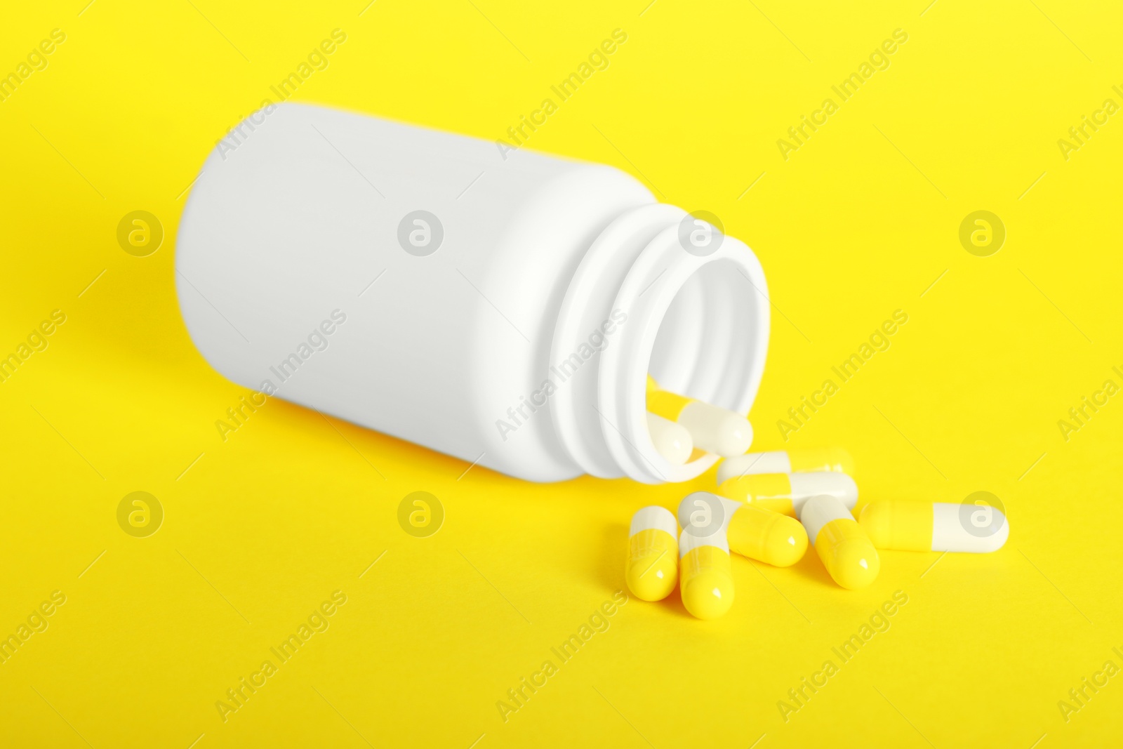 Photo of Scattered antibiotic pills and bottle on yellow background. Medicinal treatment