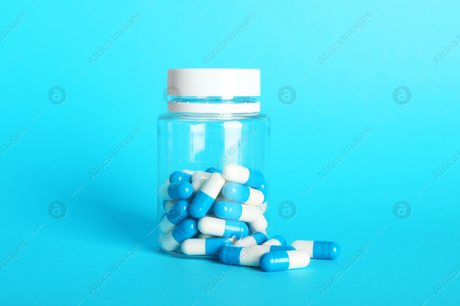 Photo of Antibiotic pills and bottle on light blue background. Medicinal treatment