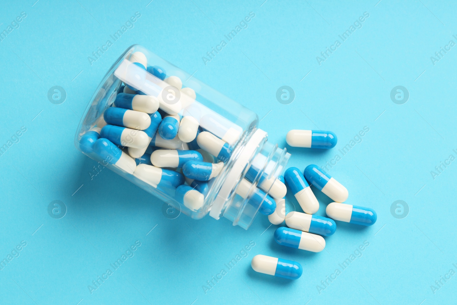 Photo of Scattered antibiotic pills and bottle on light blue background, top view. Medicinal treatment