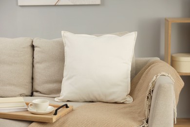 Photo of Soft white pillow, blanket and books on sofa indoors