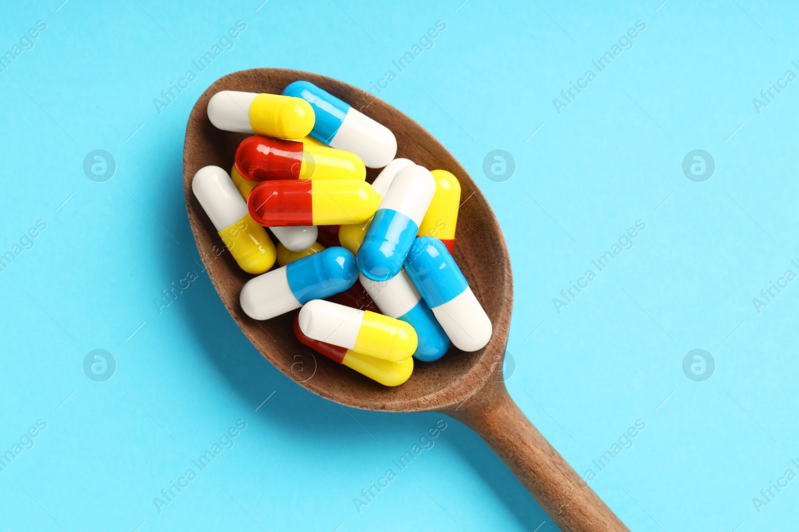 Photo of Many antibiotic pills with wooden spoon on light blue background, top view. Medicinal treatment