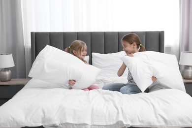 Cute little sisters having pillow fight on bed at home