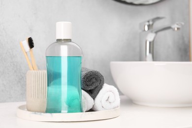 Photo of Bottle of mouthwash, toothbrushes and towels on white table in bathroom, space for text