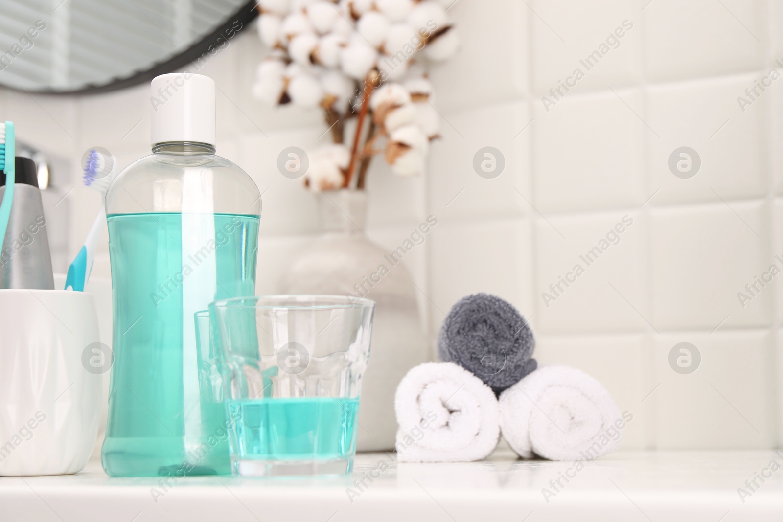 Photo of Bottle of mouthwash and glass on white table in bathroom, space for text
