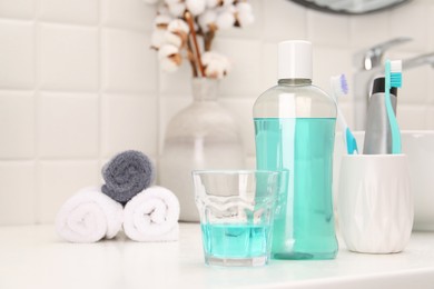 Photo of Bottle of mouthwash and glass on white table in bathroom, space for text