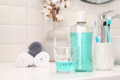 Bottle of mouthwash and glass on white table in bathroom, space for text