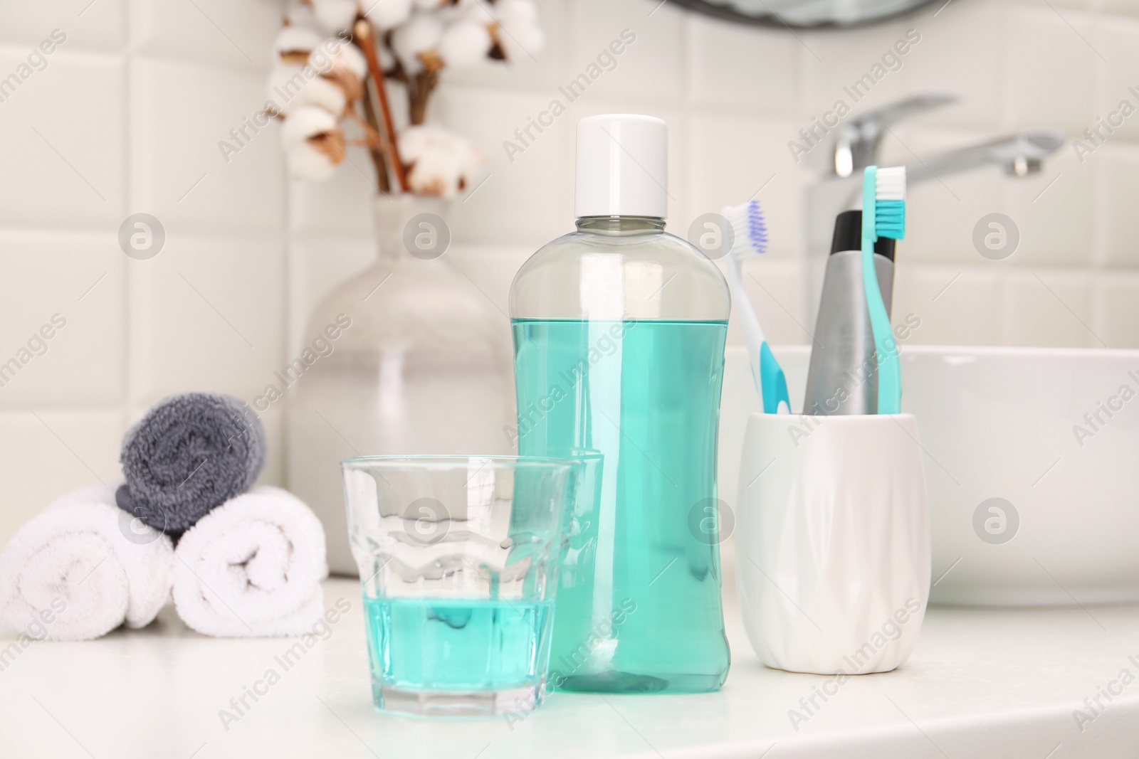 Photo of Bottle of mouthwash and glass on white table in bathroom