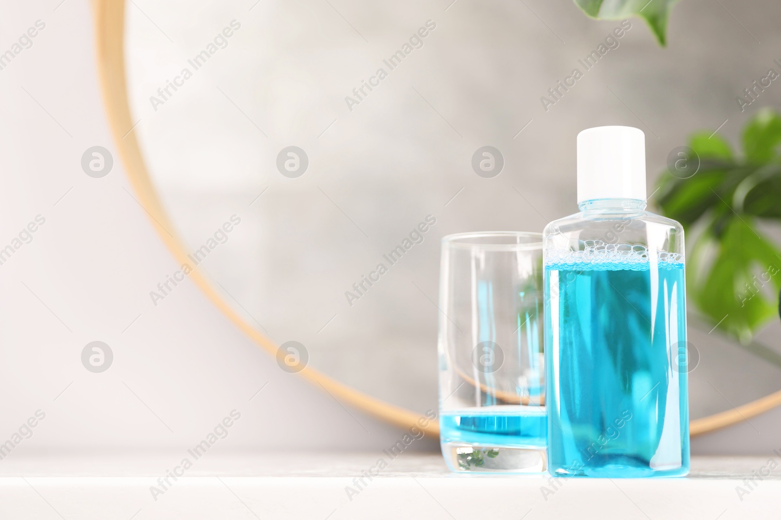 Photo of Bottle of mouthwash and glass on white table in bathroom, space for text