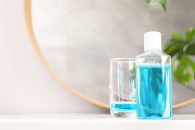 Bottle of mouthwash and glass on white table in bathroom, space for text