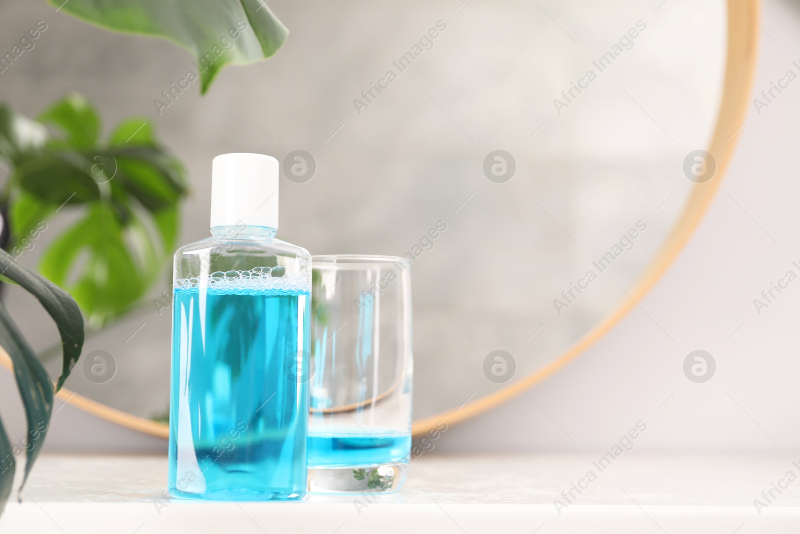 Photo of Bottle of mouthwash and glass on white table in bathroom, space for text