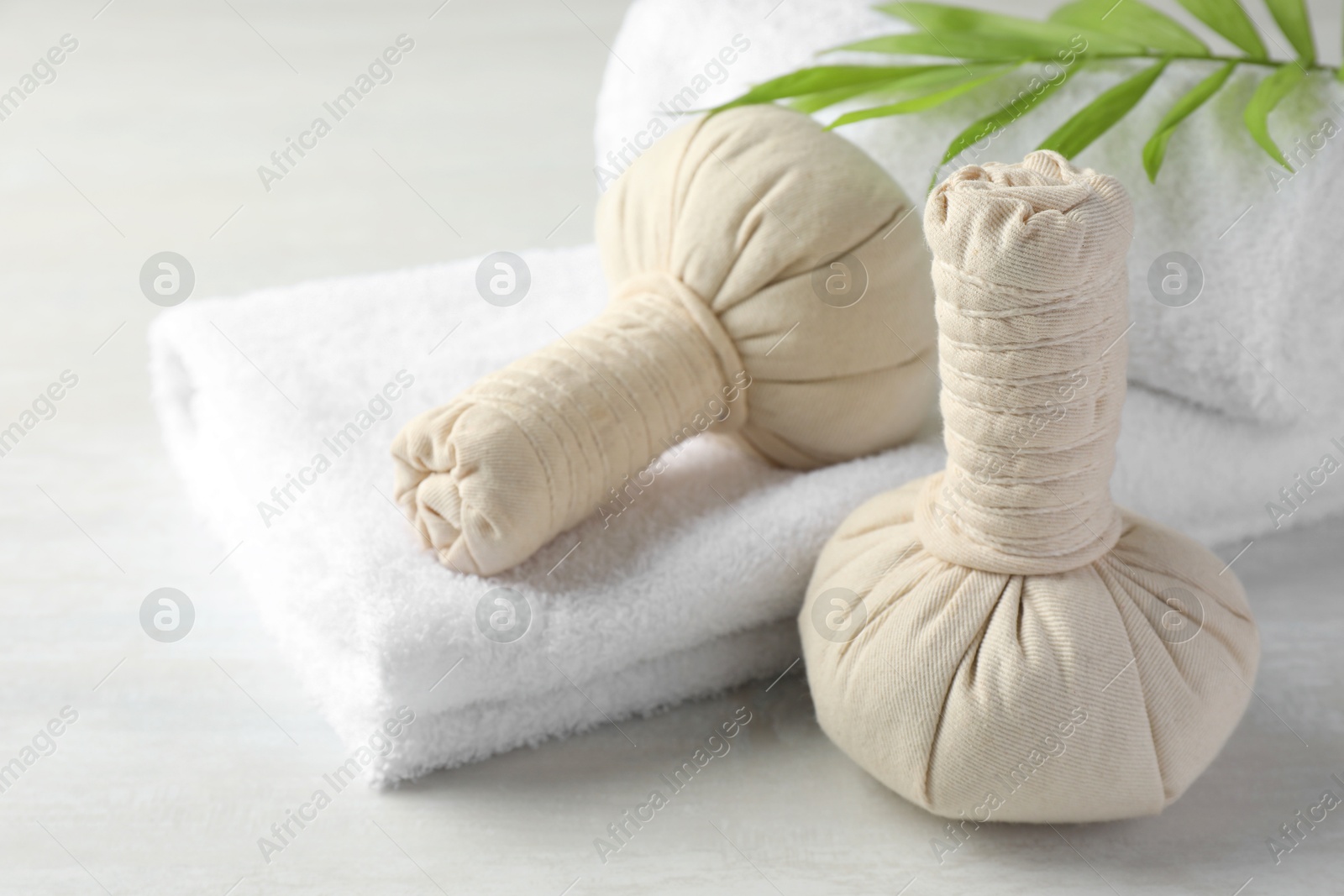 Photo of Spa composition. Herbal bags, towels and palm leaf on light table