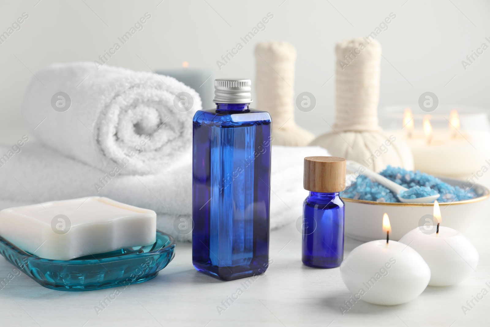 Photo of Spa composition. Cosmetic products, soap, towels, sea salt and burning candles on light table